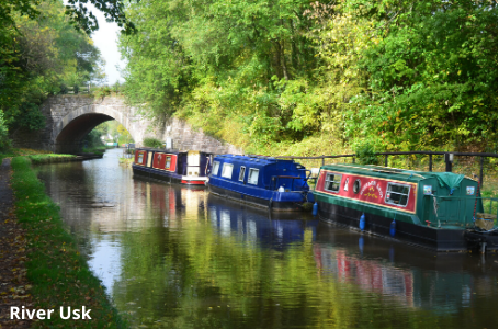 Narrowboats sit on the river on the Usk Valley Walk